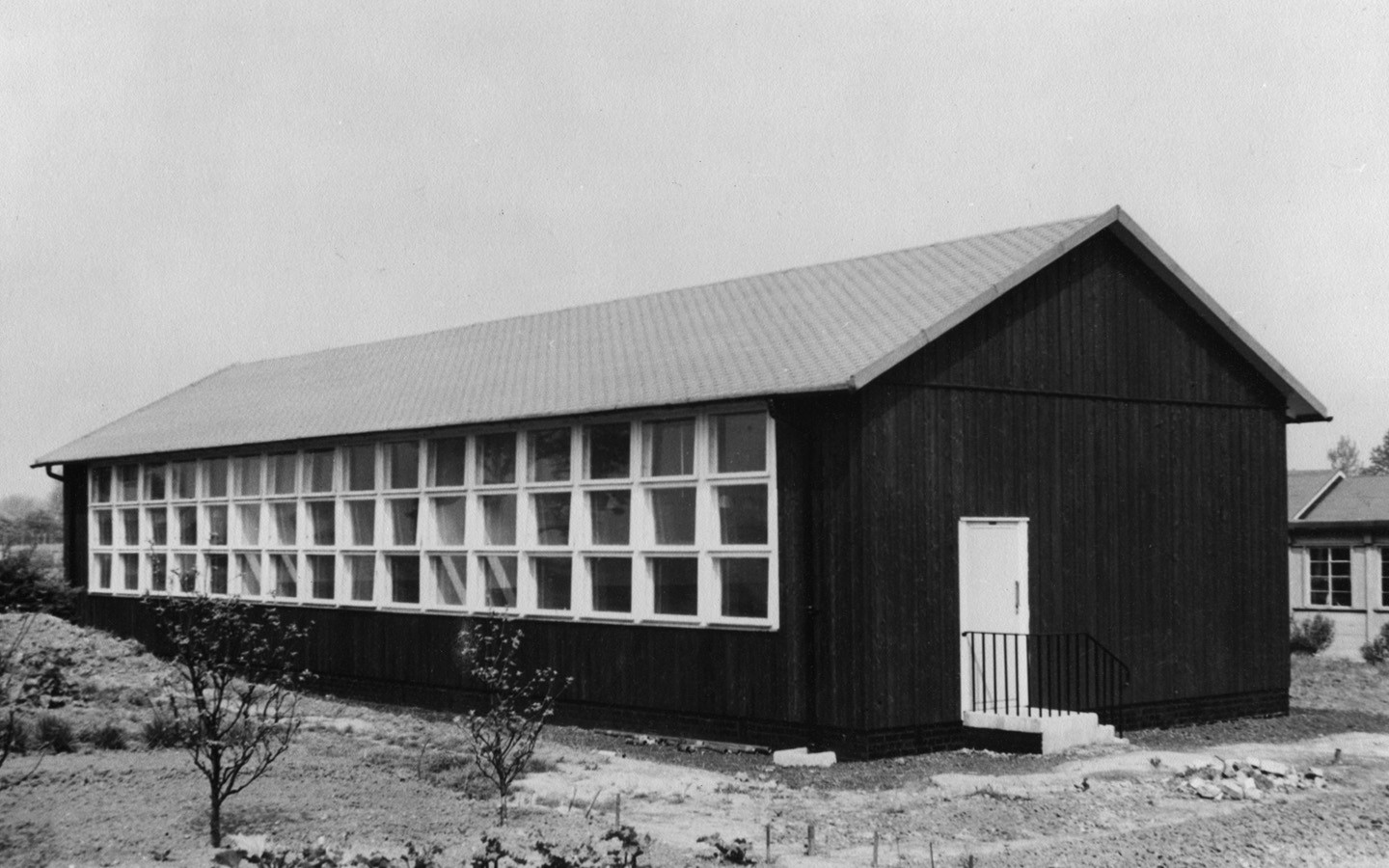 An old black and white photo of a wooden Puutalo school. On the wall there are 3 rows of windows with 16 windows in each.