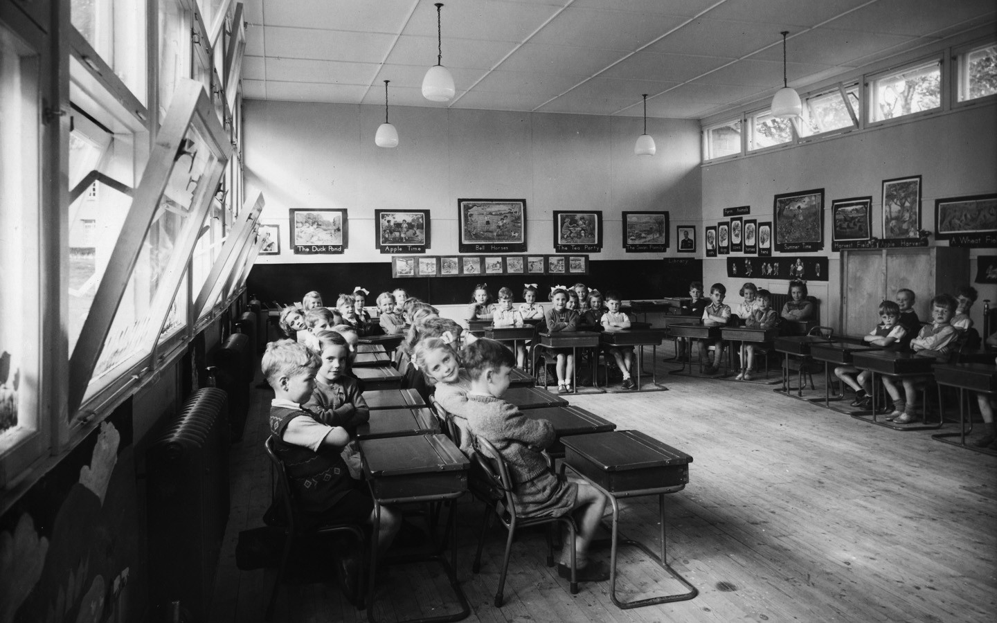 An old black and white photo of a class room where there are children sitting at their desks.