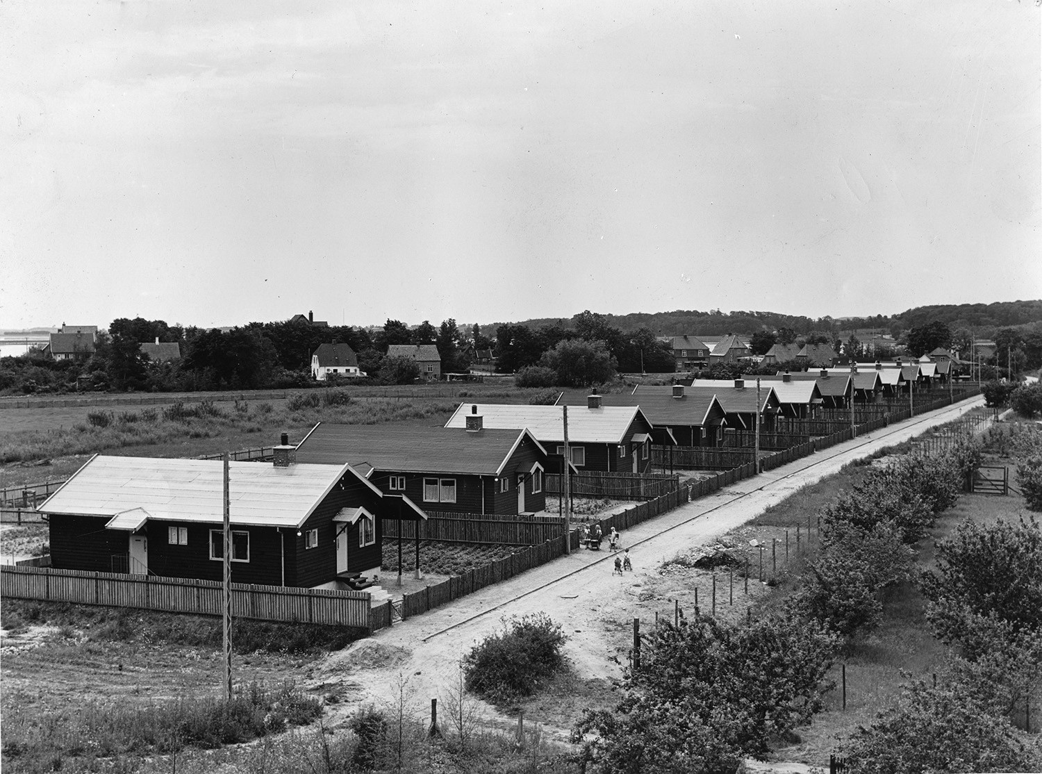 A black and white photo of a street with Puutalo Oy's detached houses on adjacent fenced plots.