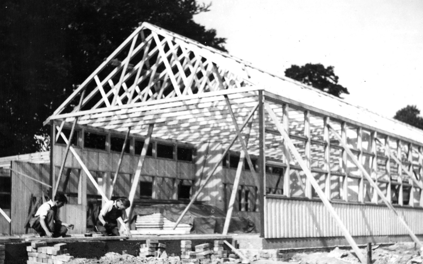 An old black and white picture of a Puutalo school under construction. The frame and roof crest are up.